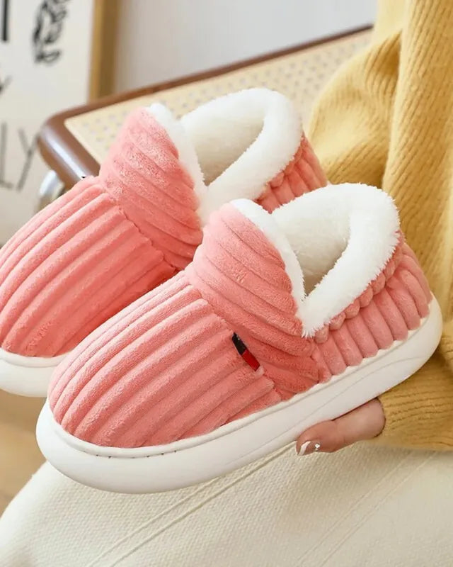 A hand holding a pink pair by the fleece collar, showing the white sole