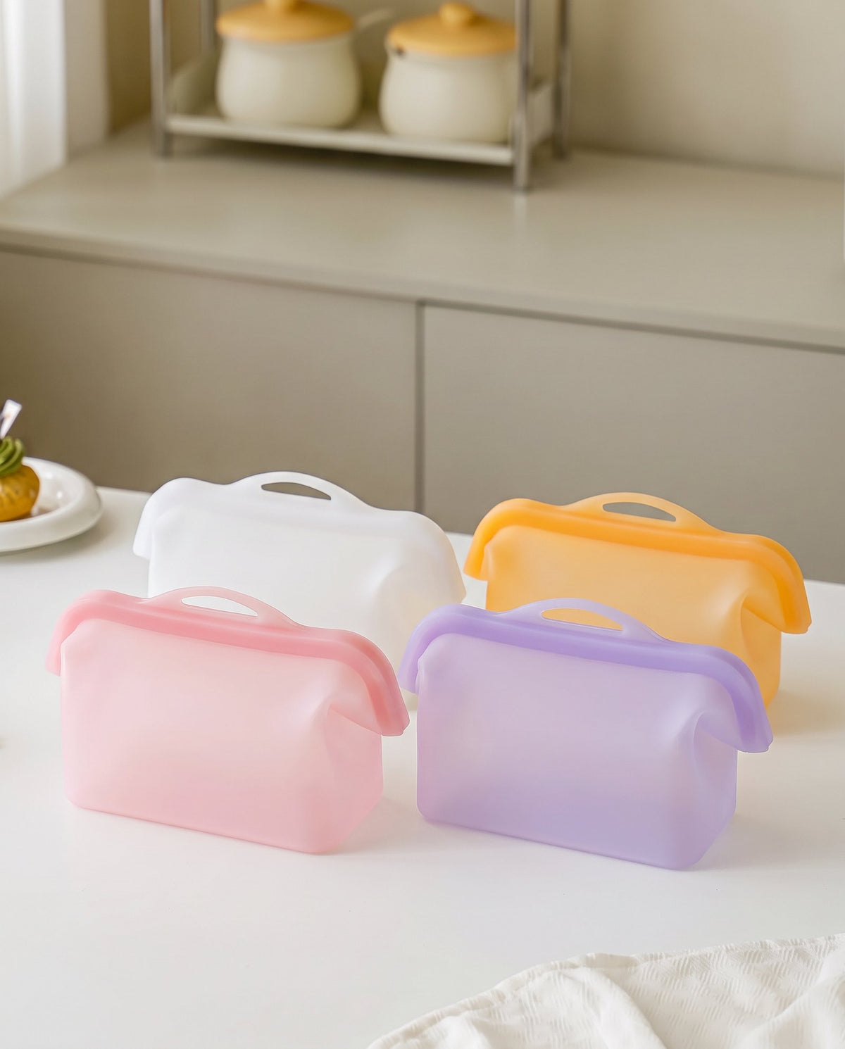 Four silicone storage bags in Blush, Cloud, Apricot and Periwinkle standing on a kitchen table
